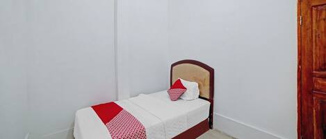A small, single-bed room with a wooden headboard, white walls, and a wooden door.