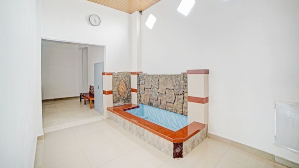 A room with a stone headboard, a wooden bench, a clock, and a door leading to another room. - Hotel O Sepakat Guest House (Medan)