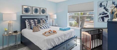 A bedroom with a bed, bedside tables, a crib, and artwork on the walls.