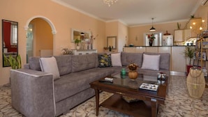 A living room with a grey sofa, a glass coffee table, and a chandelier. - Antigoni s Family House - Antigoni s Family House (Zakynthos)