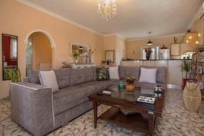 A living room with a grey sofa, a glass coffee table, and a chandelier.