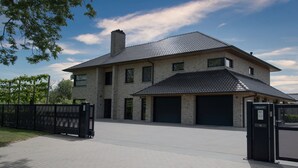 A two-story house with a garage, a brick exterior, and a metal roof. - Casa Tibella is an attractively furnished holiday home. (Ichtegem)