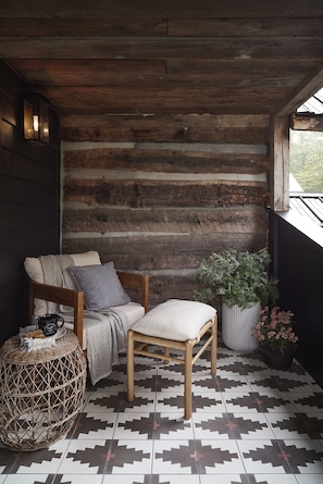 Un rincón acogedor con un banco de madera, un sillón con cojines, una cesta tejida y una planta en maceta.
