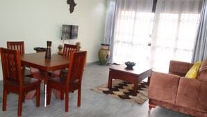 A dining area with a wooden table and chairs, a sofa, and a decorative vase. - NL JOSEPHINES APARTMENTS (Kampala)