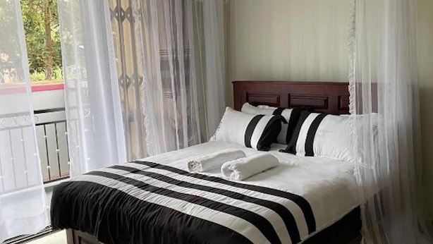 A bed with a canopy, white bedding, and a black and white striped bedspread. - NL JOSEPHINES APARTMENTS (Kampala)