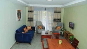 A living room with a blue sofa, two armchairs, a wooden dining table, and a coffee table. - NL JOSEPHINES APARTMENTS (Kampala)