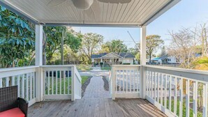 A covered porch with a wooden deck, white railings, and a pathway leading to a house.