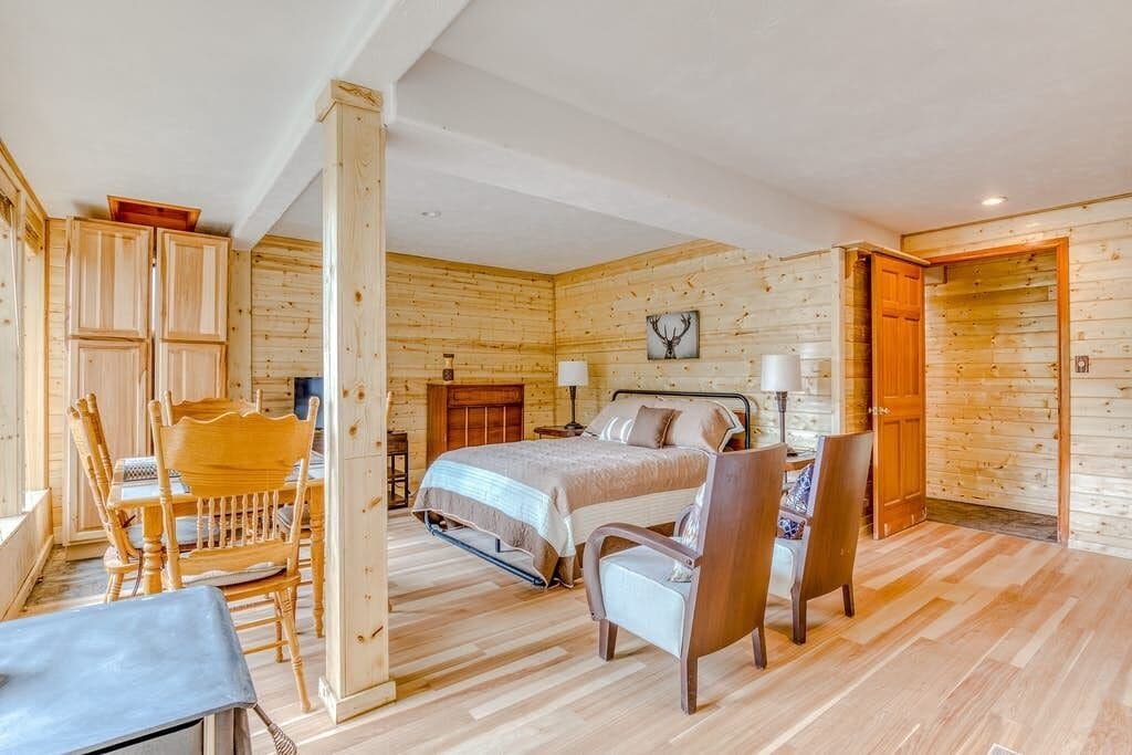Ein gemütliches Schlafzimmer in einer Blockhütte mit einem Bett, zwei Stühlen, einem Tisch und einem Holzschrank.