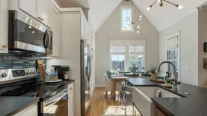 A modern kitchen with stainless steel appliances, a dining area with a table and chairs, and a large window providing natural light. - Dog Friendly Home in Carlton Landing | Blue Haven (Carlton Landing,)