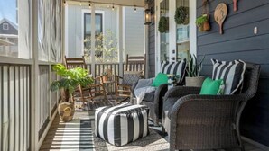 A covered porch with wicker furniture, a striped ottoman, and a 'welcome' sign. - Dog Friendly Home in Carlton Landing | Blue Haven (Carlton Landing,)