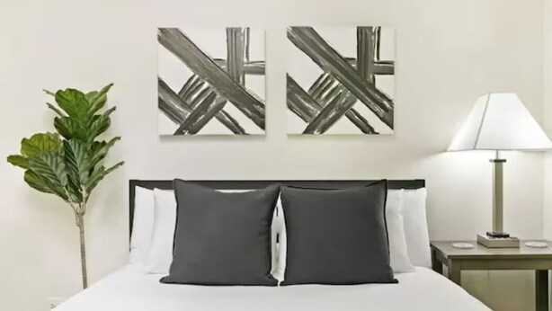Ein Hotelzimmer mit einem Bett, zwei Kissen, einem Nachttisch mit Lampe und zwei abstrakten Bildern an der Wand.