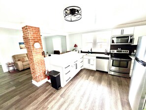 A modern kitchen with white cabinets, a brick accent wall, a built-in oven, and a microwave.