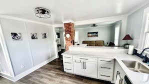 Une cuisine moderne avec des meubles blancs, un îlot central et un mur d’accent en briques.