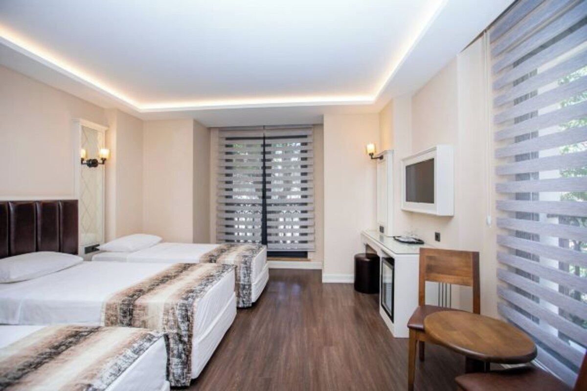 A hotel room with two beds, a desk with a chair, a TV, and a window with blinds.
