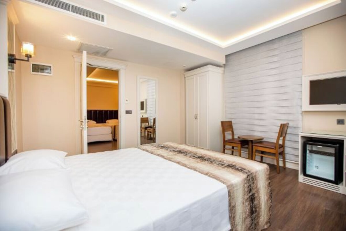 A hotel room with a bed, a desk, a chair, a TV, and a fireplace.