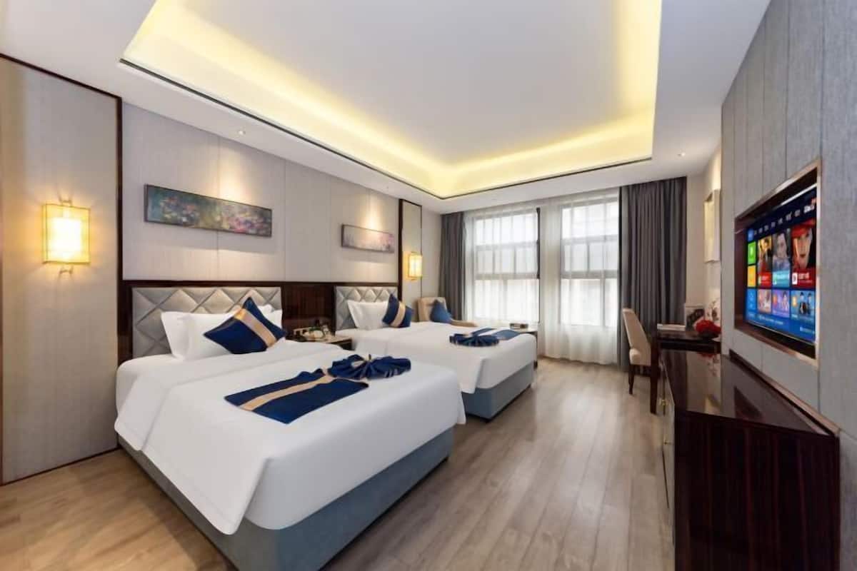 Una habitació d'hotel amb dos llits, una televisió, una taula de treball i un finestral gran.