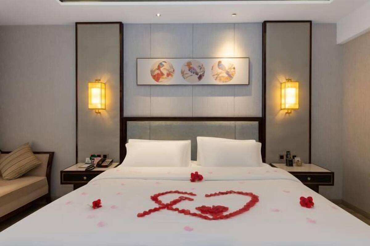 Habitació d'hotel amb un llit gran, dues taules de nit, un calbó, un sofà i una obra d'art penjada a la paret.