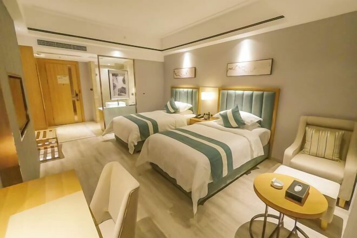 Hotellihuone, jossa on kaksi sänkyä, pieni pyöreä pöytä, tuoli ja sohva.