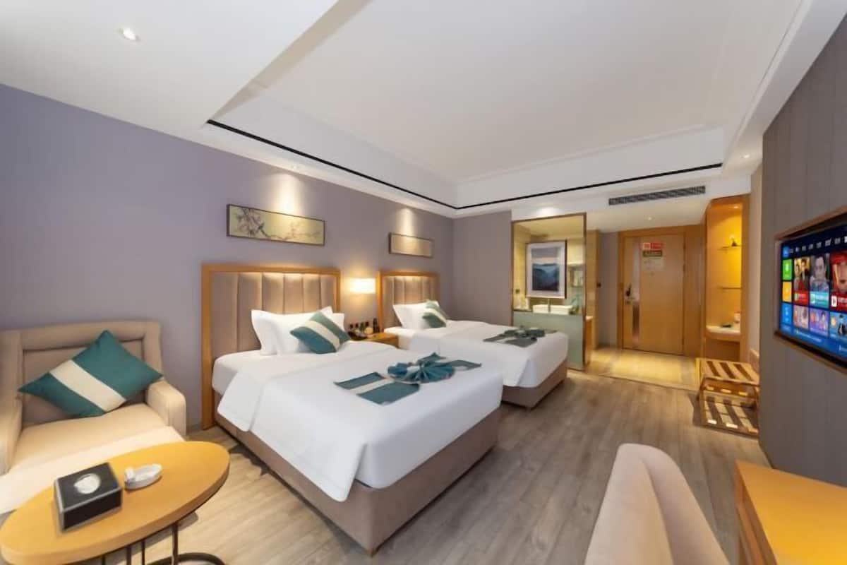 Habitació d'hotel amb dos llits, un sofà, una taula petita i una televisió.