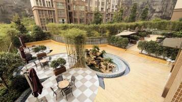 A rooftop garden with outdoor seating, a circular water feature, and a view of a mountainous landscape.