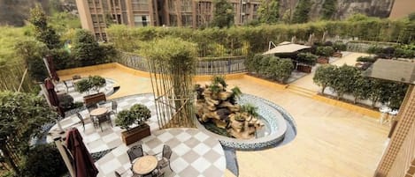 A rooftop garden with outdoor seating, a circular water feature, and a view of a mountainous landscape.
