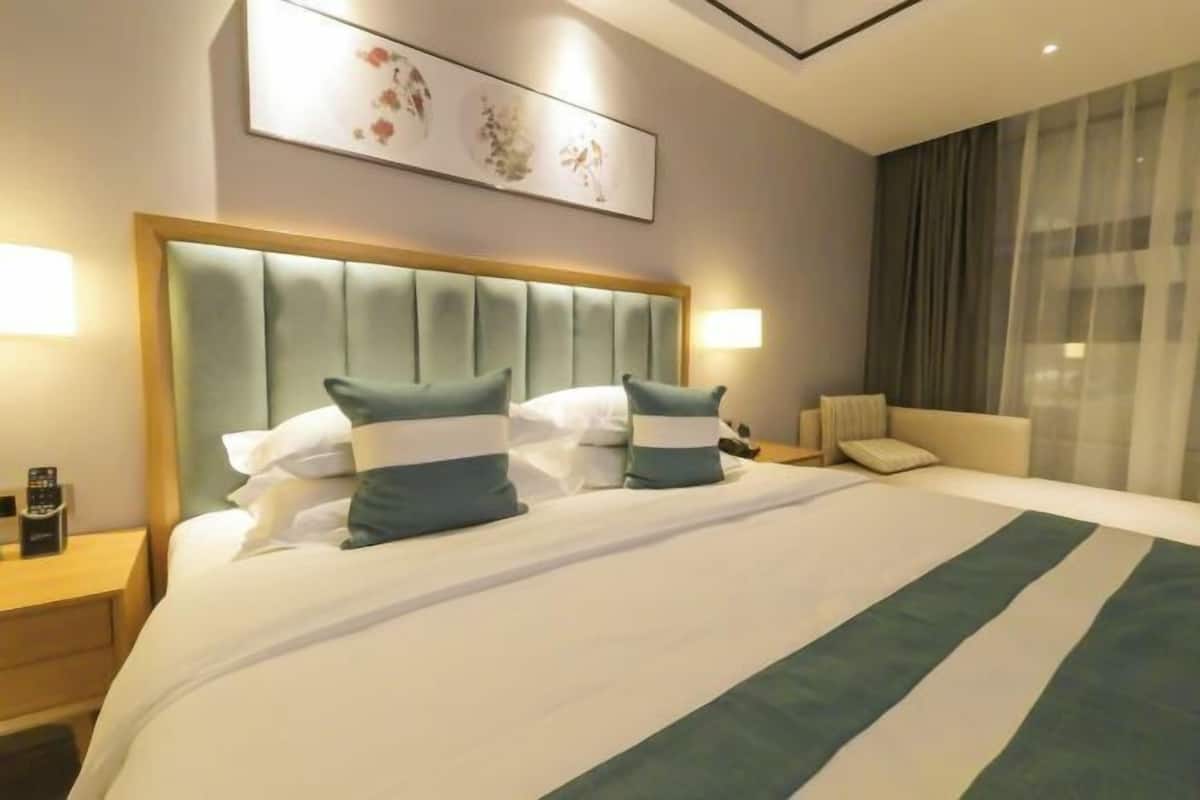 Habitació d'hotel amb un llit gran, un capçal, una taula de nit i una làmpada. Hi ha una finestra amb cortines.