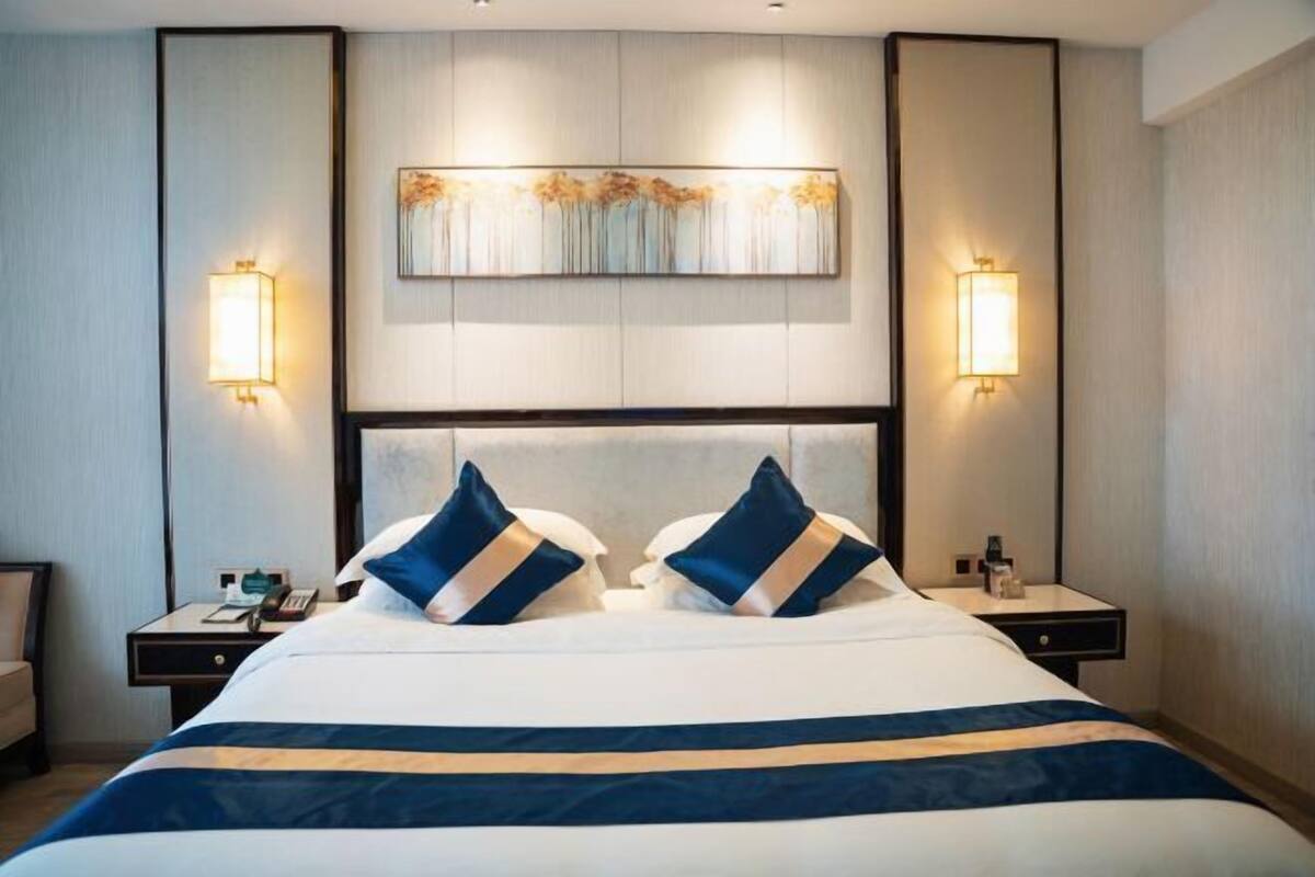 Habitació d'hotel amb un llit gran, dues taules de nit, una obra d'art penjada a la paret i dues làmpades de paret.