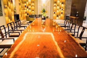 Una larga mesa de conferencias de madera con sillas, rodeada de estanterías con objetos decorativos y un sofá al fondo.