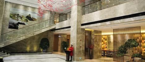 A spacious lobby with a marble floor, a grand staircase, and a reception area with a staff member.
