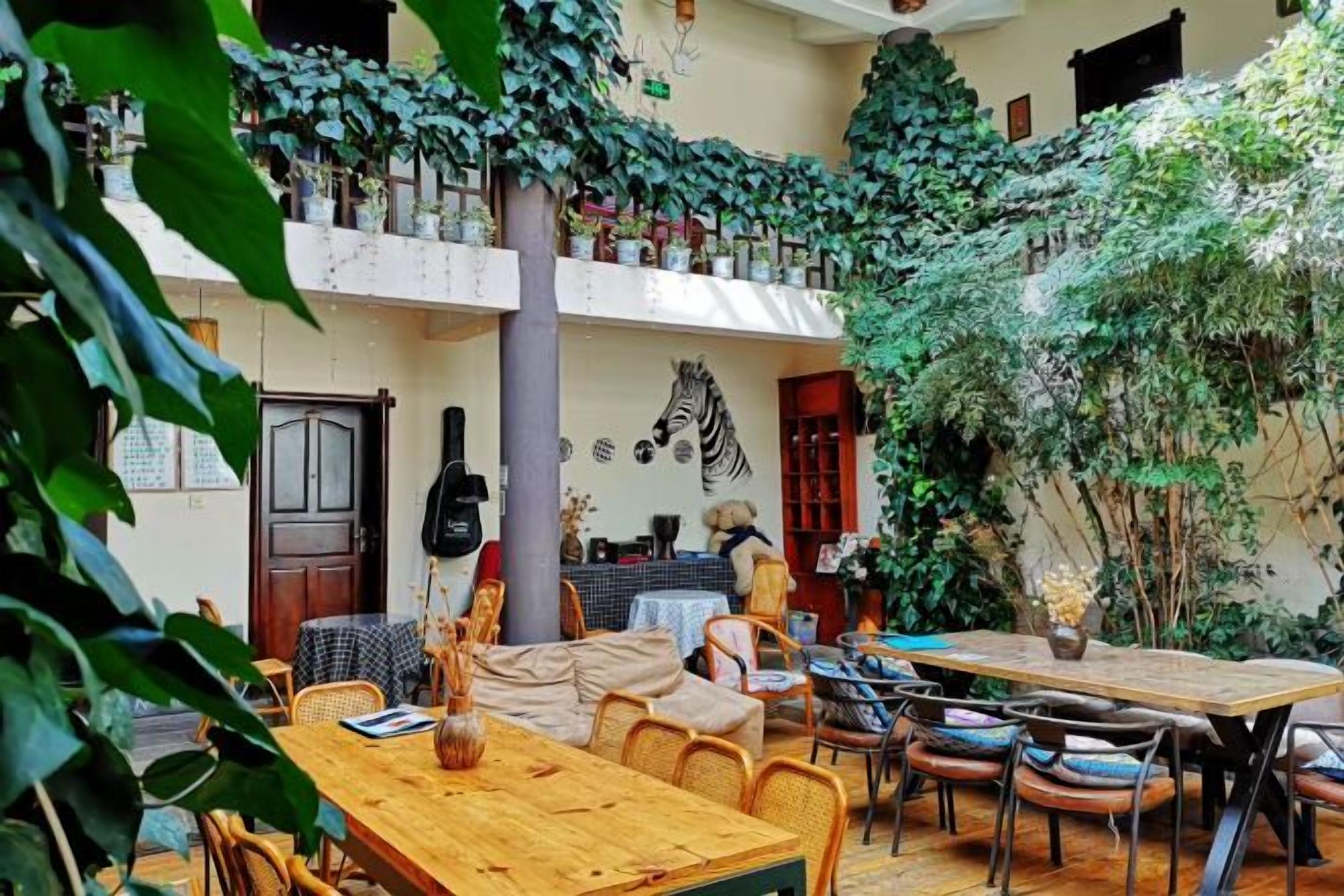A cozy outdoor dining area with wooden tables and chairs, surrounded by lush greenery and a tiled floor.