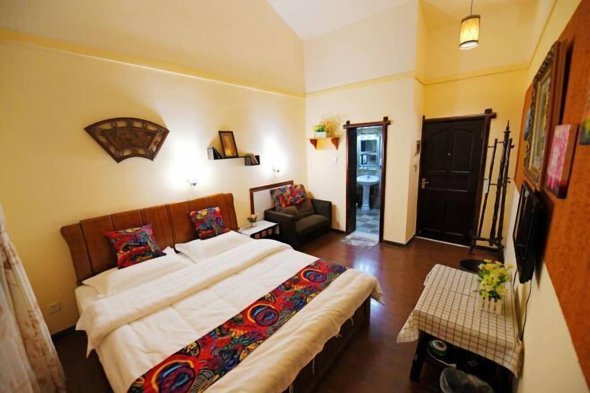 A bedroom with a large bed, a small table with a checkered tablecloth, and a door leading to a bathroom.