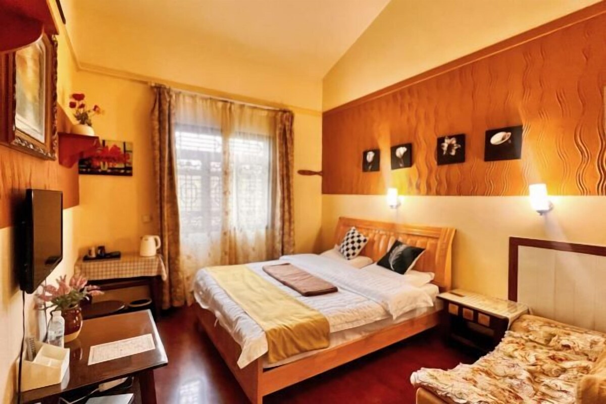 A hotel room with a bed, bedside table, lamp, curtains, and a wall-mounted TV.