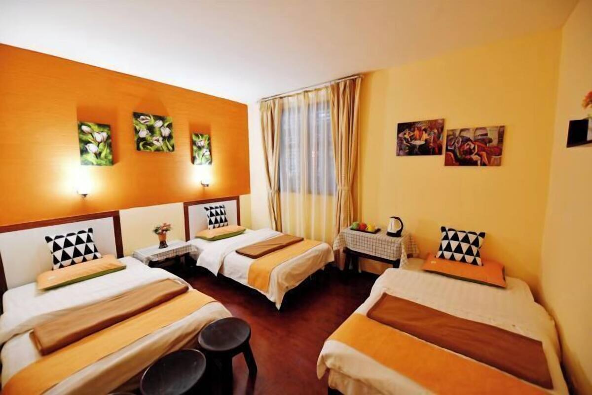 A hotel room with two beds, a small table with a fruit bowl, and artwork on the walls.