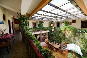 A spacious indoor area with a high ceiling, wooden beams, and a variety of plants. There are multiple seating areas and a staircase leading to an upper level. - Maple Leaf Inn Lijiang (Lijiang)