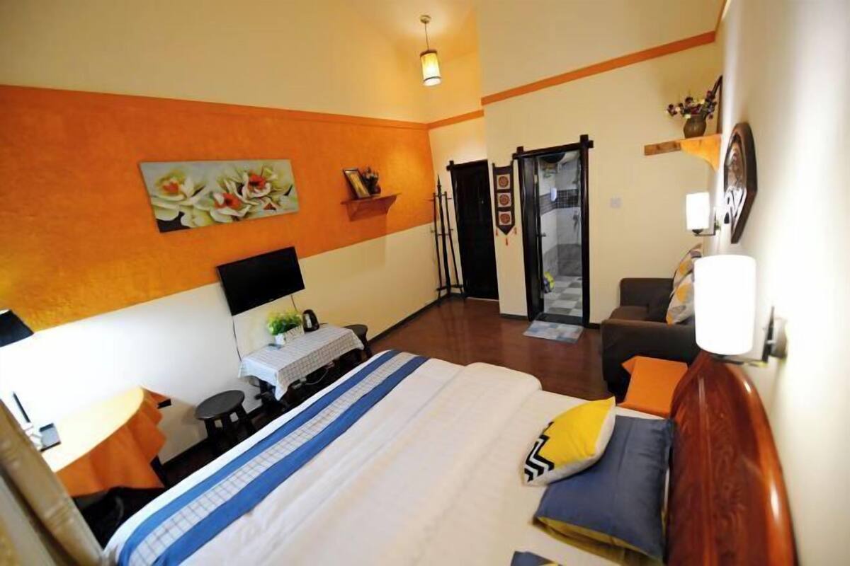 A hotel room with a bed, a desk with a computer, a chair, a sofa, and a small table with a plant.