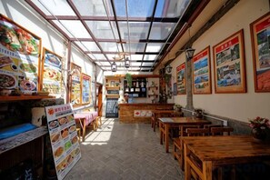 A restaurant with a high ceiling, wooden tables, and chairs, and a menu board on the left. - Maple Leaf Inn Lijiang (Lijiang)