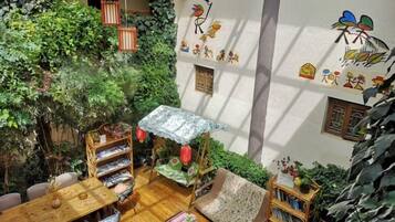 A cozy indoor space with a wooden table, chairs, a patterned sofa, and a small garden area with plants and a decorative umbrella.