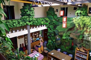 Una stanza con una grande libreria, una scrivania e un affresco raffigurante una foresta.