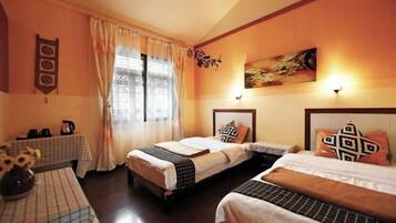 A hotel room with two beds, a table with a checkered tablecloth, a vase with flowers, and a painting on the wall.