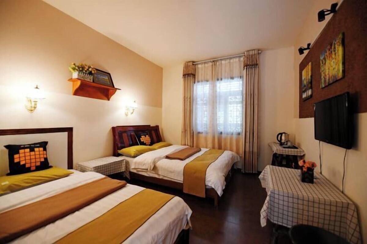 A hotel room with two beds, a small table, a TV, and a window with curtains.