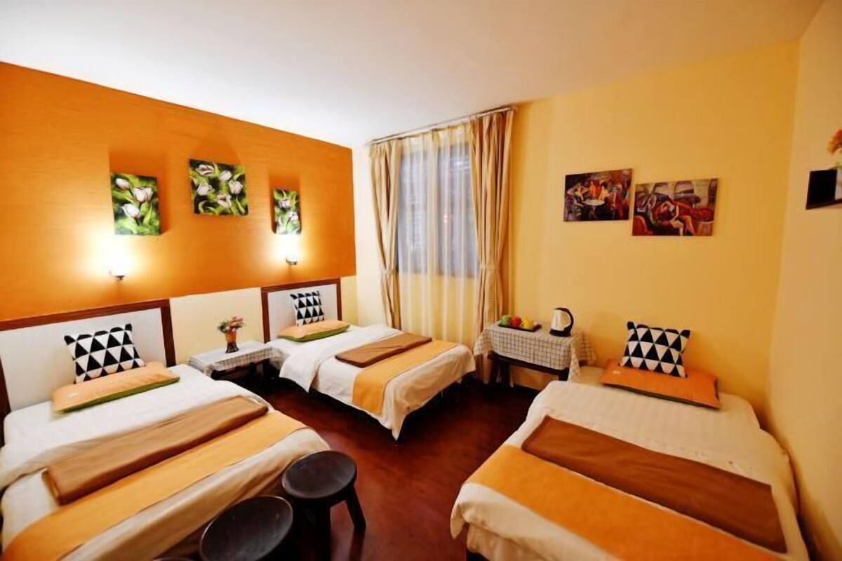 A hotel room with two beds, a small table with a fruit bowl, and artwork on the walls.