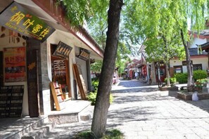 A tree-lined street with traditional architecture, including a shop with a sign in a foreign language. - Maple Leaf Inn Lijiang (Lijiang)