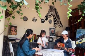 A room with a table, chairs, and a person playing a guitar. - Maple Leaf Inn Lijiang (Lijiang)