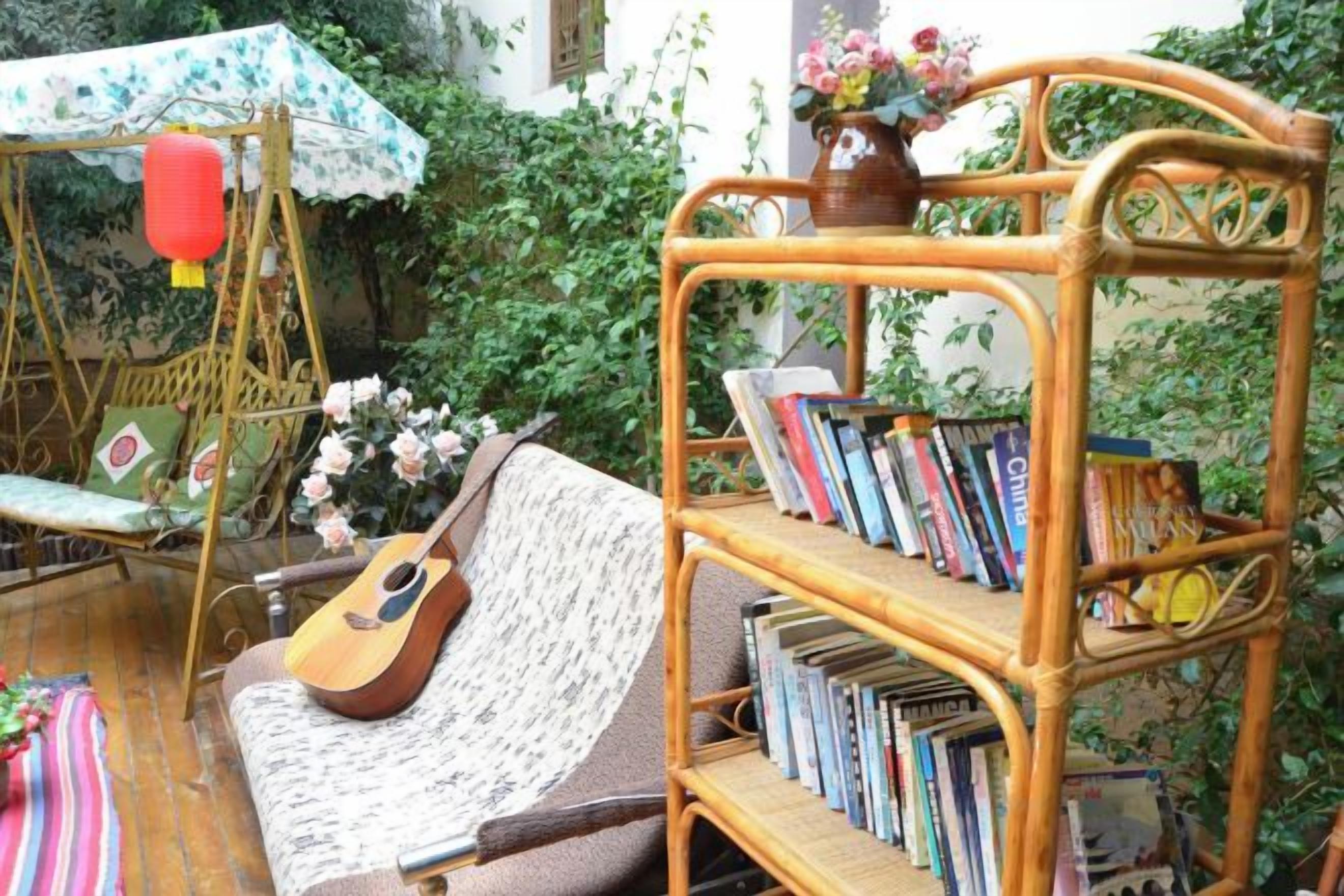 Une bibliothèque en osier remplie de livres, un fauteuil suspendu en osier et un canapé en osier avec une guitare.