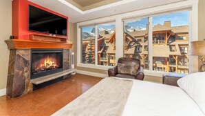 Quarto com lareira, televisão, janela ampla e vista para as montanhas, e uma cama.