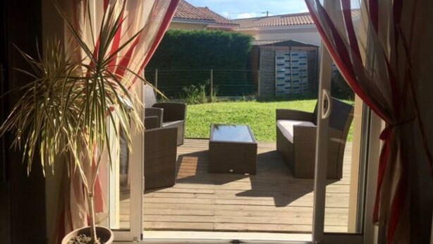A view through a glass door into a patio area with a wooden deck, a potted plant, and outdoor furniture.