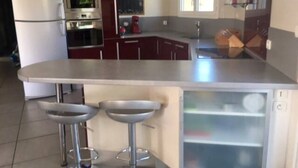 A kitchen with a stainless steel island, two bar stools, a refrigerator, an oven, and a microwave.