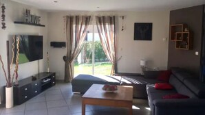 A modern living room with a flat-screen TV, a sofa, a coffee table, and a large window with curtains.