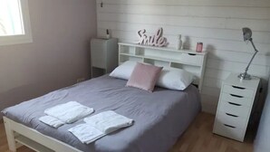 A neatly made bed with white linens, a bedside table with a lamp, and a shelf with decorative items.