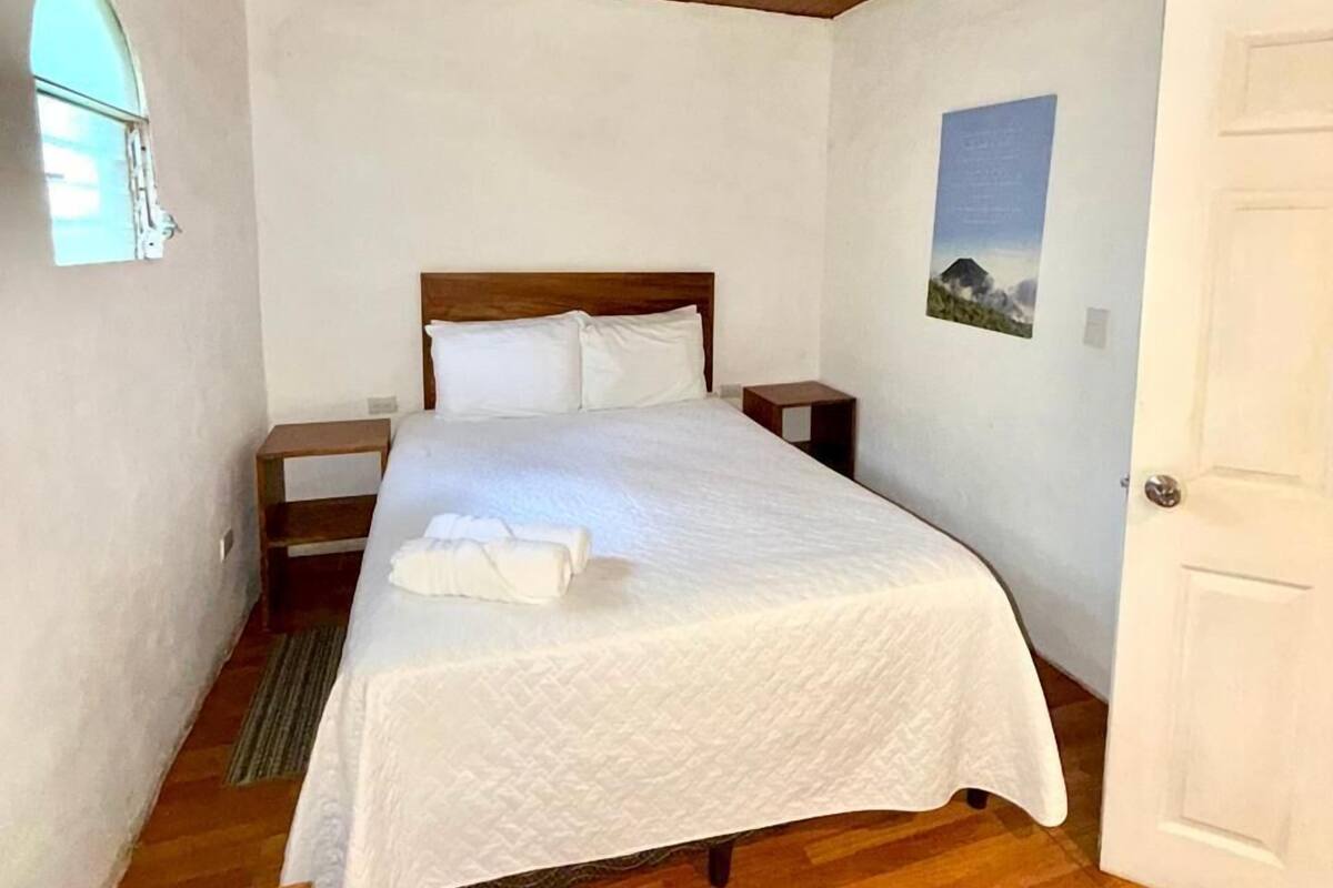 A bedroom with a wooden ceiling, a bed with white linens, a nightstand, a small table, and a door.